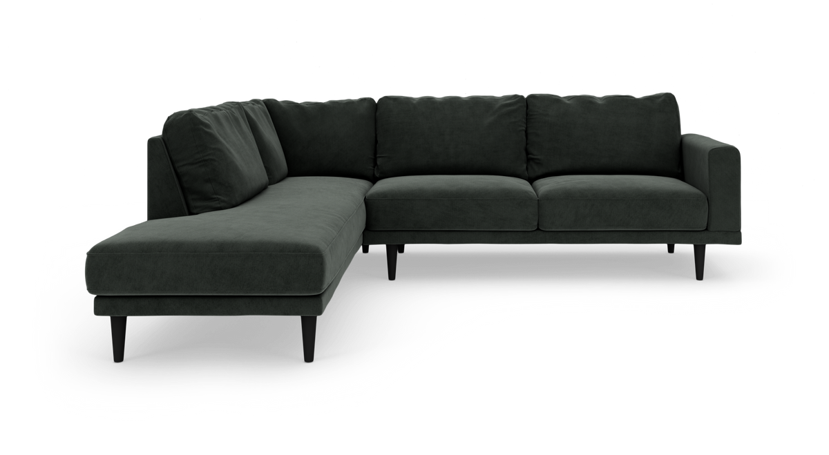 Mørkegrøn L-formet stofsofa med slanke sorte ben.