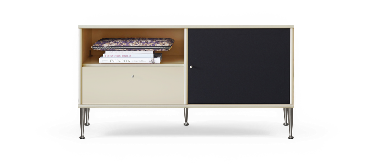 Beige skænk med metalben, åbent rum med et mønstret etui og bøgerne DESIGNERNES BOLIGER og EVERGREEN Living with Plants, nederste skuffe og sort skydedør.
