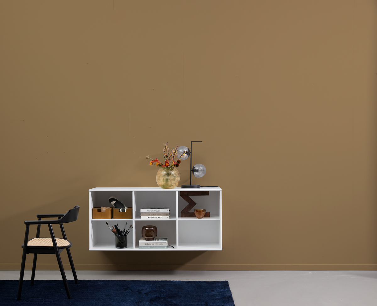 Minimalistisk stue med hvid væghylde, sort stol med fletsæde, blåt tæppe, vase med orange blomster og bordlampe med glasglober mod beige væg.
