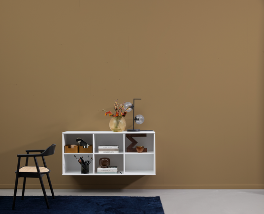 Minimalistisk stue med hvid væghylde, sort stol med fletsæde, blåt tæppe, vase med orange blomster og bordlampe med glasglober mod beige væg.