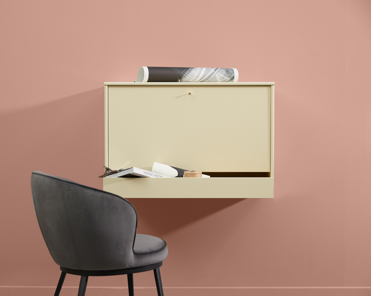 Vægmonteret beige skrivebord med åben klap, grå stol og en bog med titlen ”NORDIC MOOD”, foran en rosa væg.