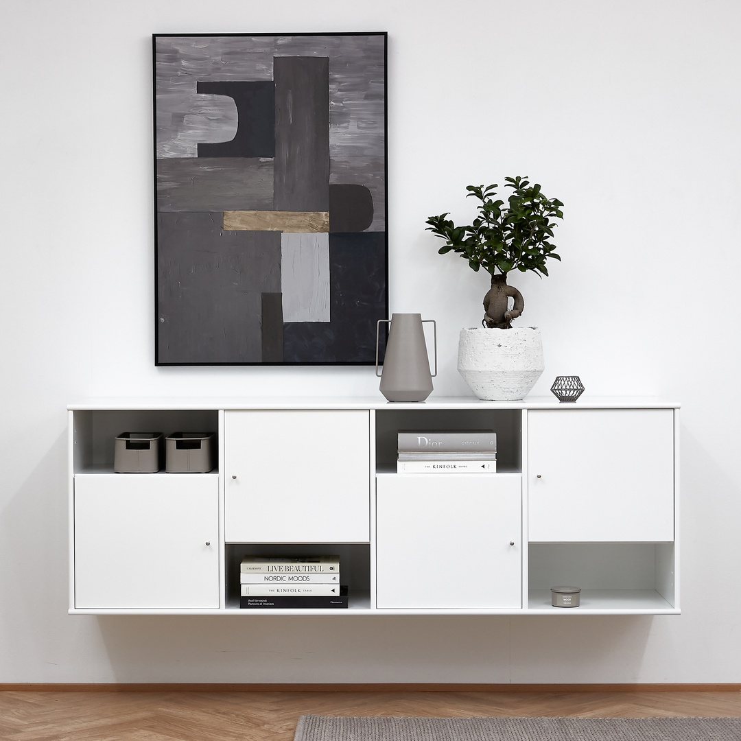 Hvid væghængt skænk med bøger (”Dior”, ”Live Beautiful”, ”Nordic Moods”, ”Kinfolk”), grå kande og grøn plante i hvid krukke; over hænger et abstrakt kunstværk i grå nuancer.