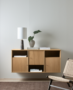 Væghængt skænk i eg med marmorbordlampe, vase med grøn bladgren og bøger – bl.a. Live Beautiful og The Kinfolk – i en minimalistisk stue med fletlounge stol og brunt tæppe.