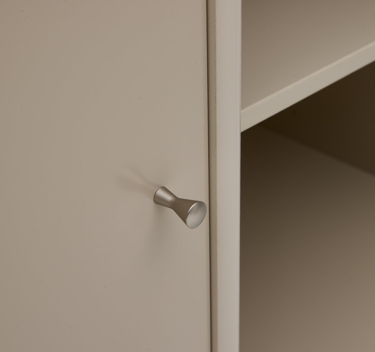 Nærbillede af beige skabslåge med sølvfarvet, kegleformet knop ved siden af et åbent hylderum.