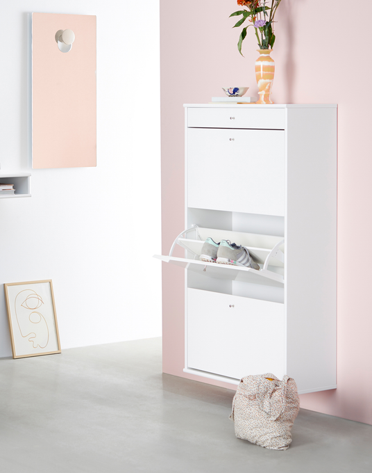 Vægmonteret hvidt skoskab med klaplåger, en låge åben med sko, mod rosa væg og en vase med blomster ovenpå.