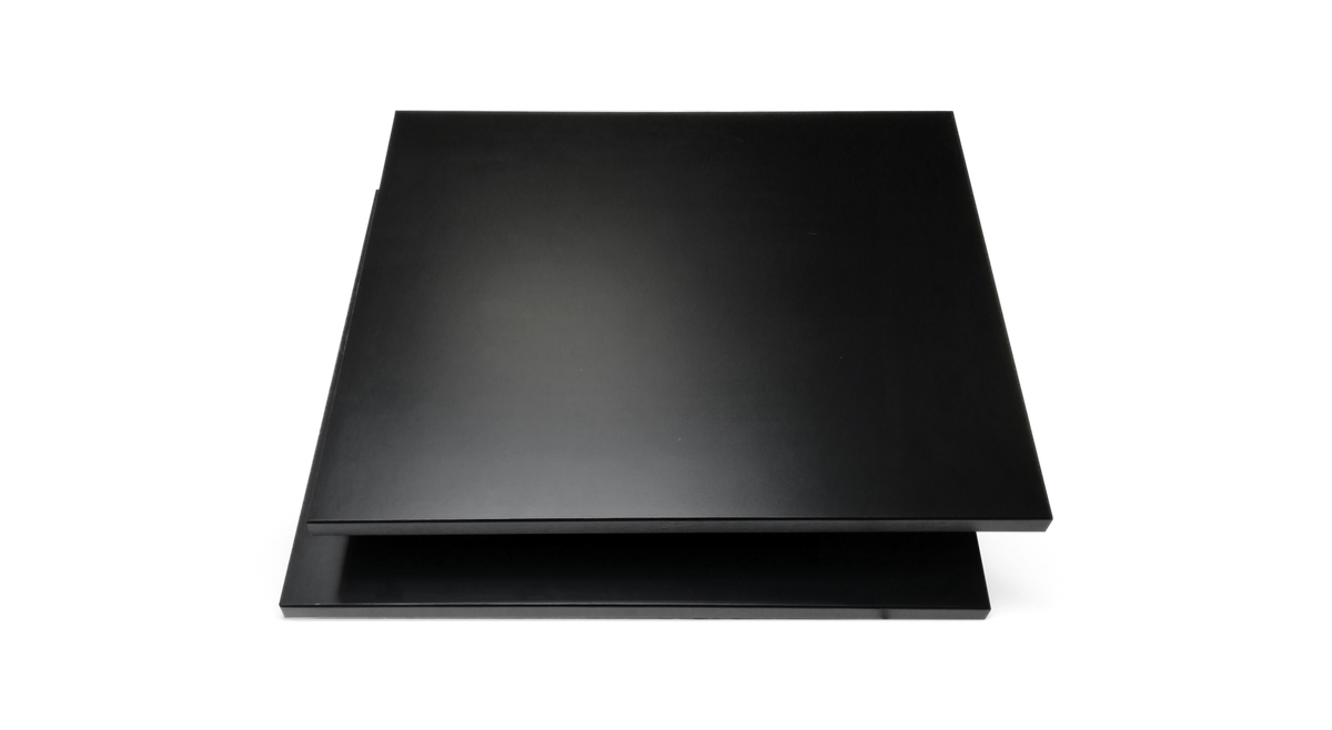 Lys skandinavisk stue med turkis hjørnesofa, sort buegulvlampe, rundt sort sofabord med bøger og vase, en grøn plante og to indrammede plakater over et beige tæppe på sildebensparket.