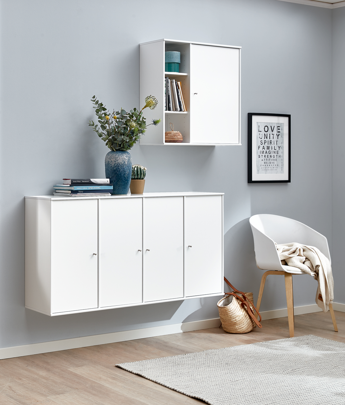 Lys, minimalistisk entré med hvide væghængte skabe, hvid stol, lyst tæppe og dekoration; LOVE, UNITY, SPIRIT, FAMILY, IMAGINE, STRENGTH, ATTITUDE på væggen; vaser med grønne grene, kurv og bøger.
