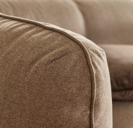 Nærbillede af beige stofsofas afrundede armlæn med synlig keder/piping.