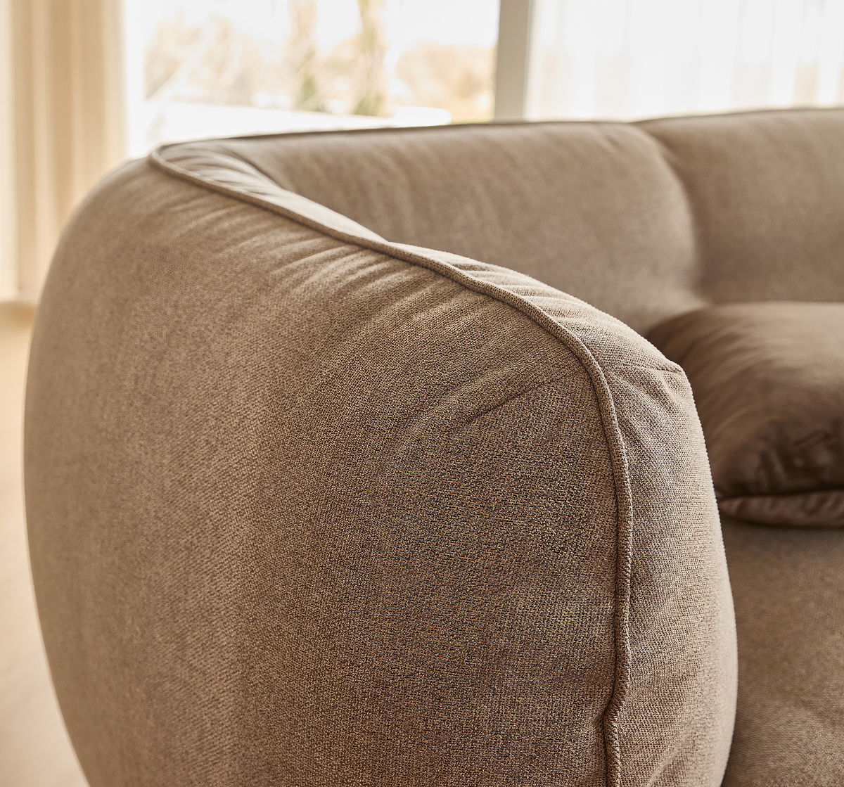 Nærbillede af rund, polstret sofaarm i beige tekstil med matchende pude i et lyst stuemiljø.
