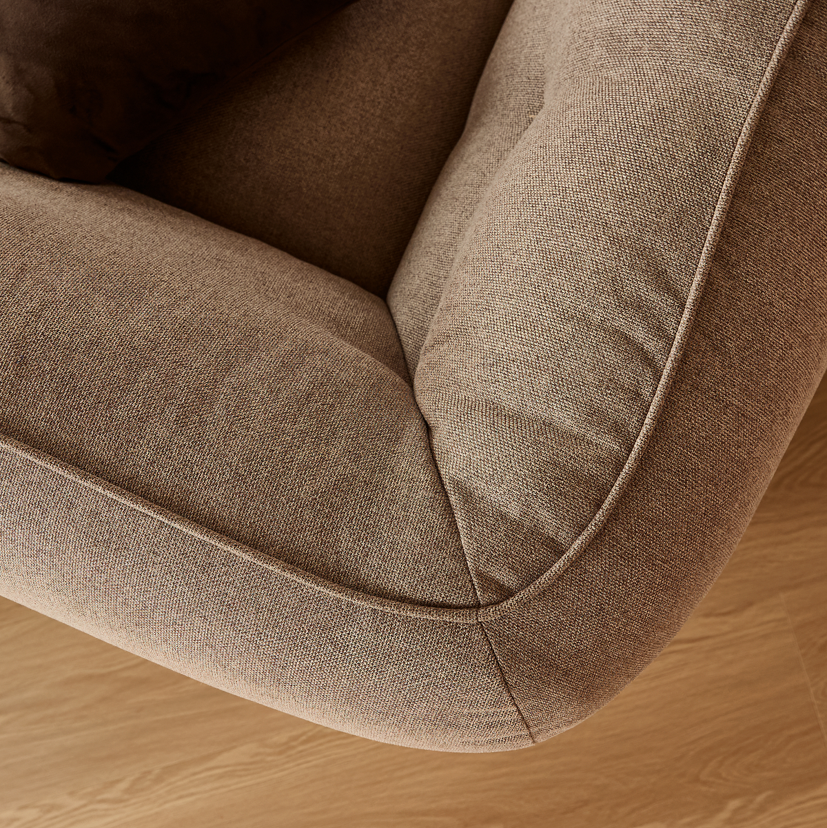Nærbillede af beige stofsofa med afrundet hjørne og pude på lyst trægulv.