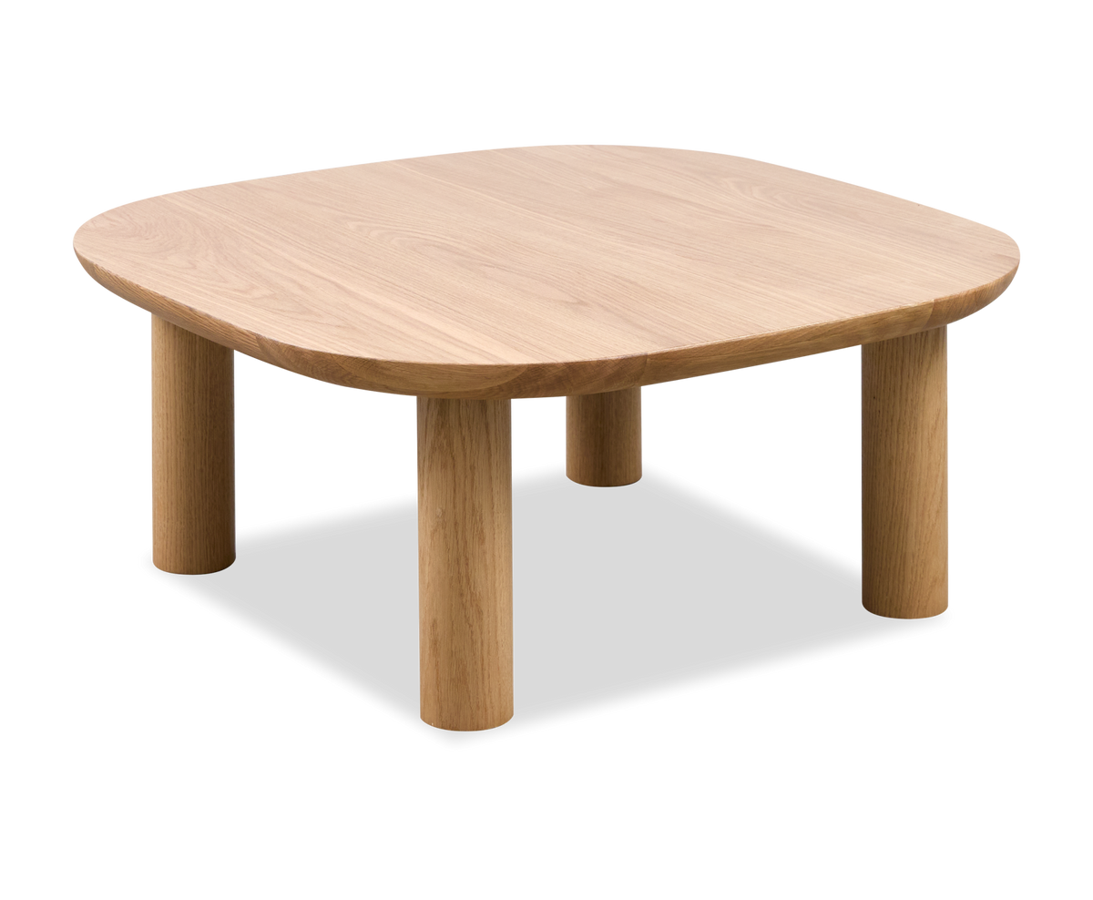 Hyggelig stue med grøn veloursofa, sofabord i træ, gallerivæg, beige tæppe og planter; blødt, varmt dagslys giver en rolig og hyggelig stemning.