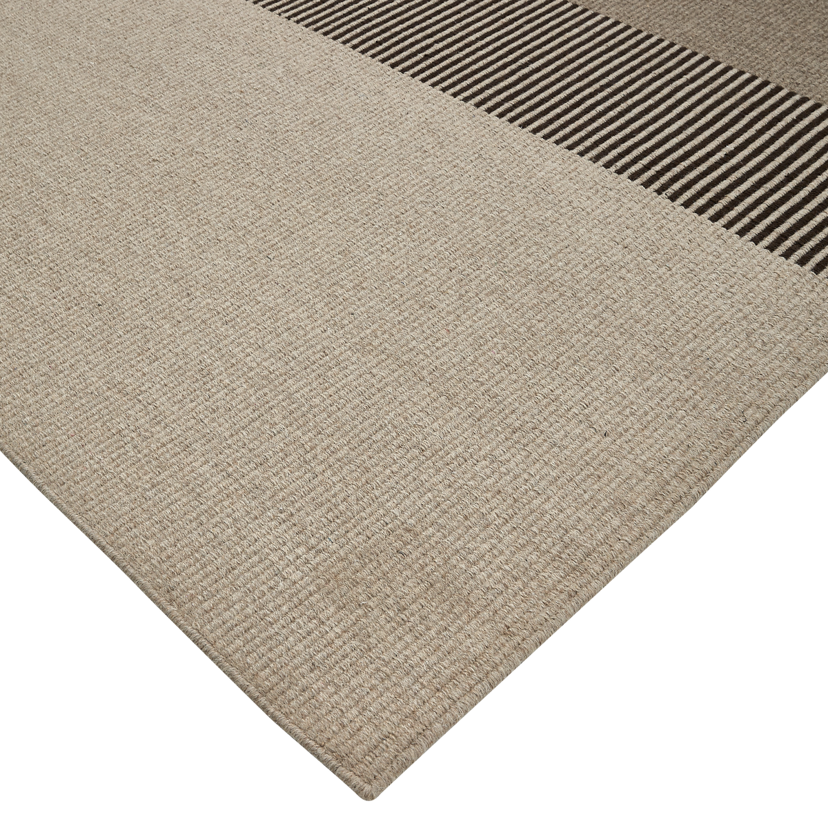 Beigefarvet fladvævet tæppe med kontrasterende mørkebrune/beige striber langs den ene kant, fotograferet fra hjørnet i studie.