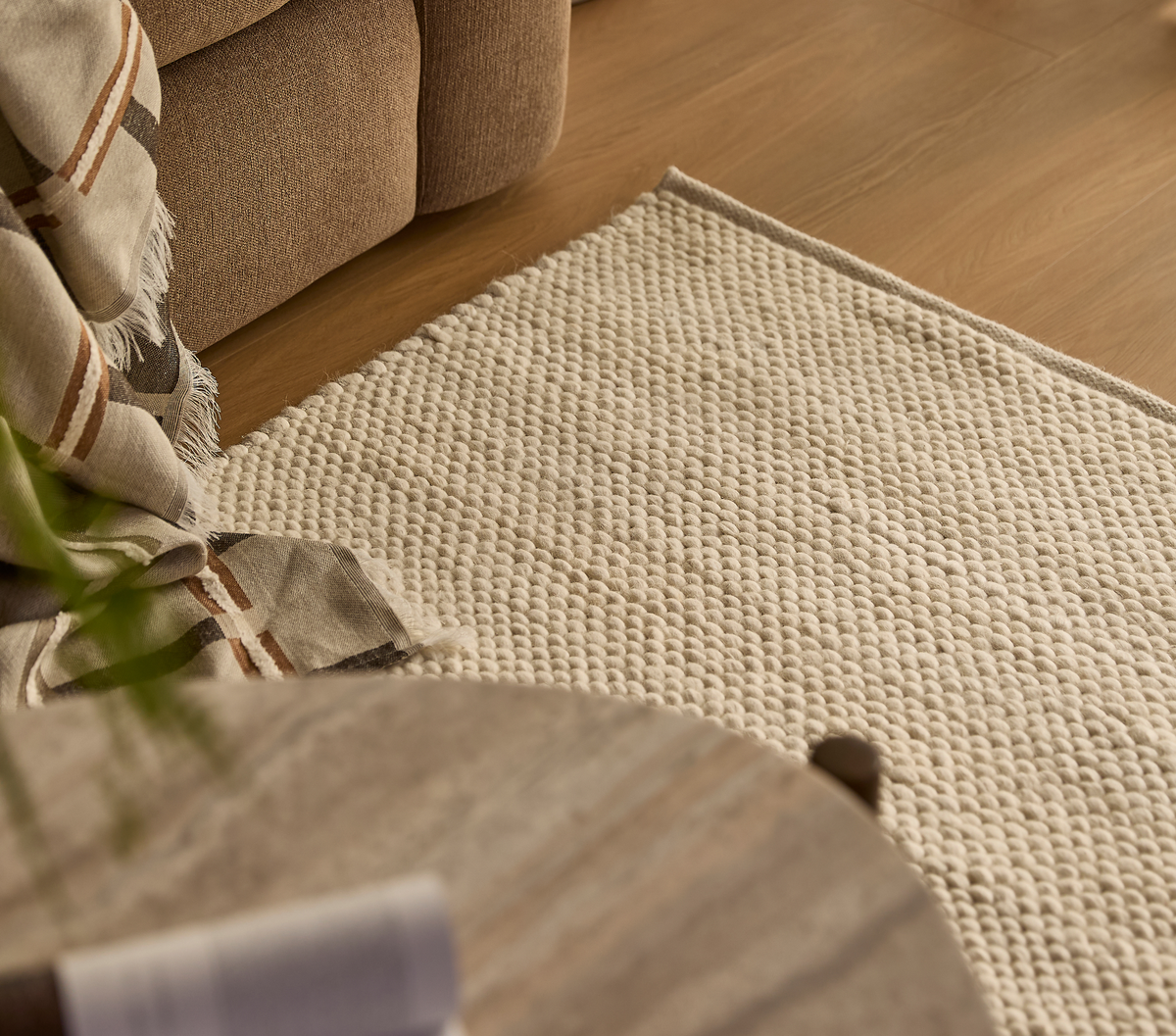 Nærbillede af beige, tekstureret tæppe ved siden af sofa med ternet plaid på trægulv i en hyggelig stue.