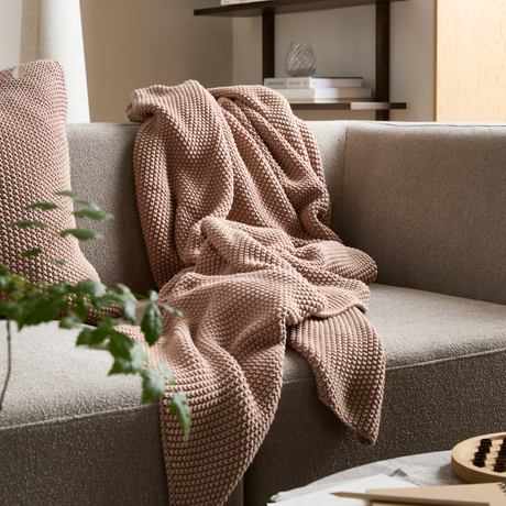 Beige sofa med rosabeige strikket plaid og matchende pude i en lys stue.