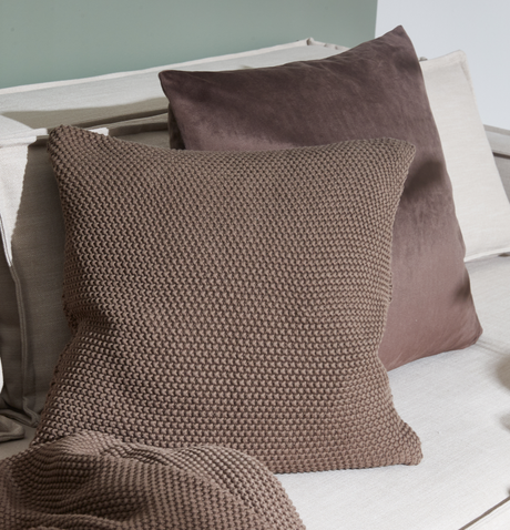 Brune puder i strikket og glat tekstur på en lys sofa, med matchende plaid.
