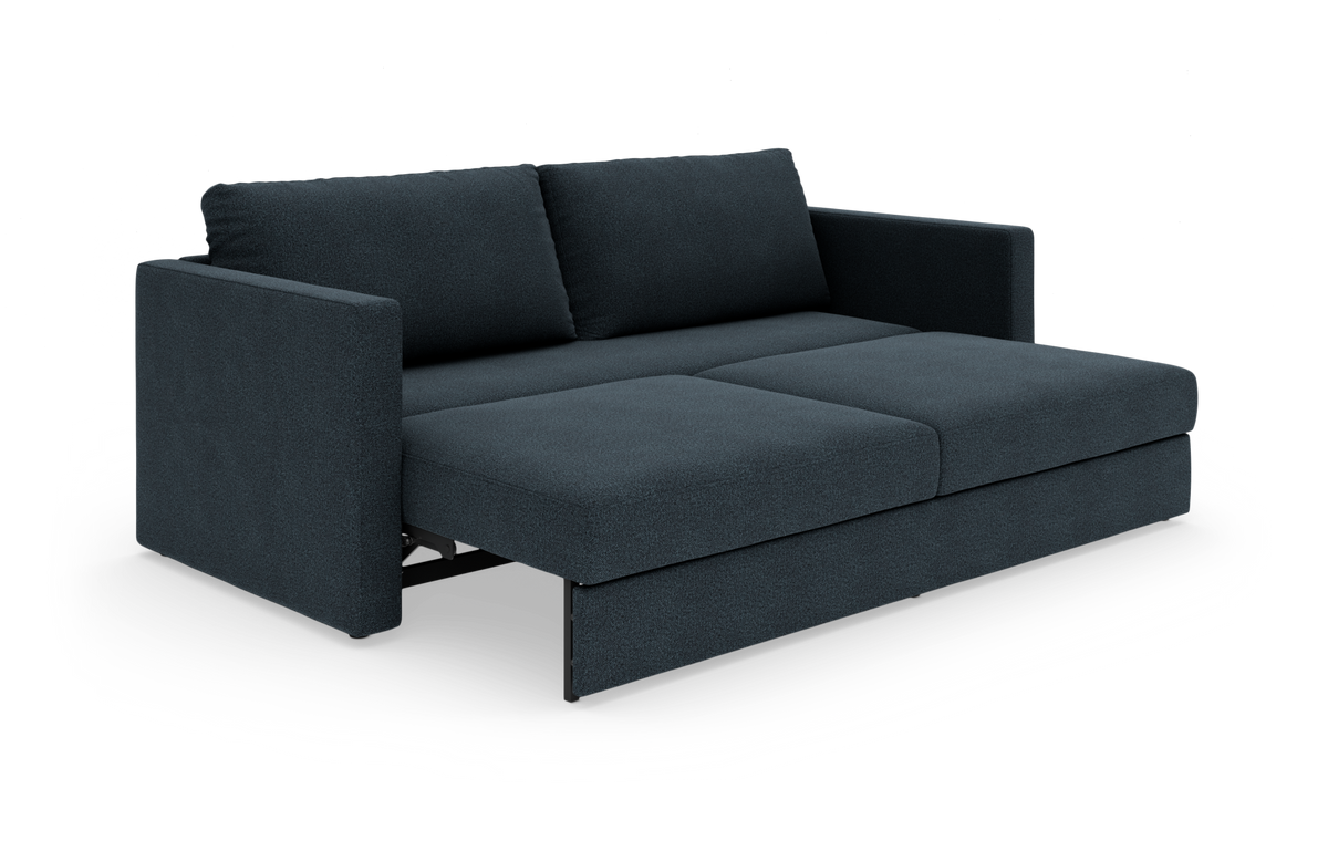 Mørkeblå sovesofa med lige armlæn og to ryghynder, fotograferet i vinkel mod hvid baggrund.