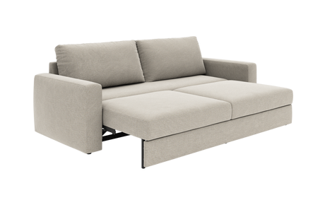 Beige sovesofa i stof, trukket ud til seng med to rygpuder, fotograferet skråt forfra.