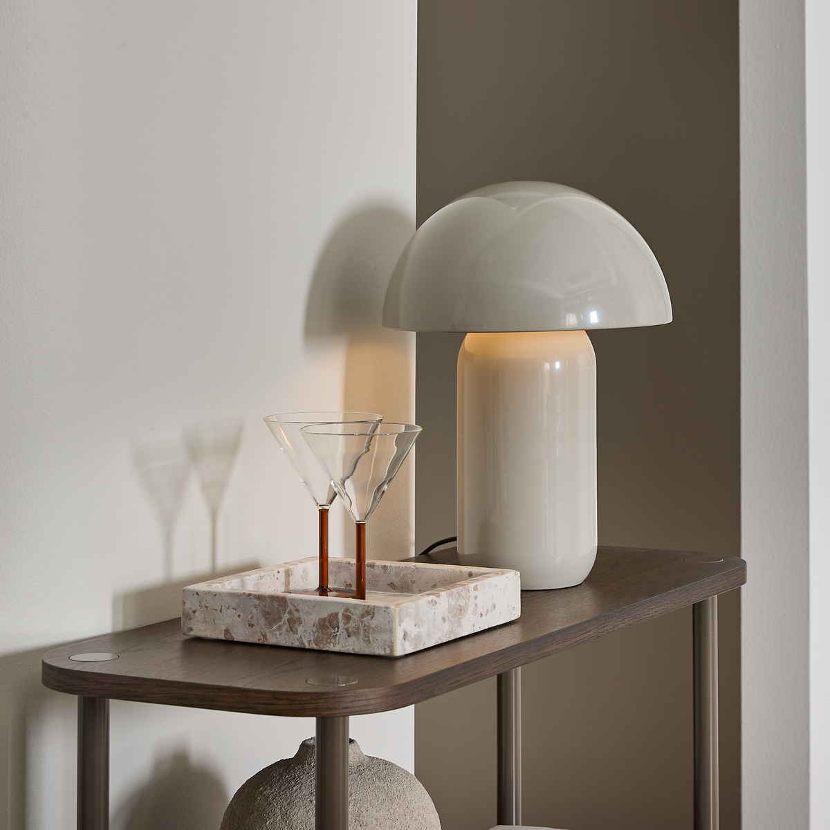 Cremehvid bordlampe på mørkt sidebord med to martini­glas i terrazzo-bakke, blødt dagslys og neutrale toner.