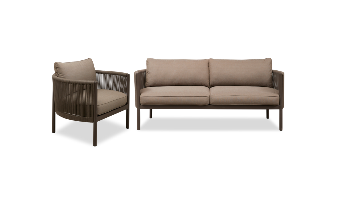Brun loungestol med rund ram, flettede sider og beige hynder, fotograferet i 3/4‑vinkel.