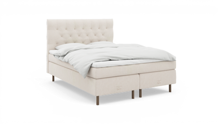 Beige polstret seng med knapstoppet sengegavl, hvid opredning og Nocturne‑branding, vist i studieoptagelse fra skrå front.