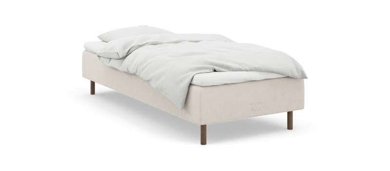Enkel seng med beige ramme, hvide sengelinned og træben, mærket ”nocturne by TEMPUR”._ps