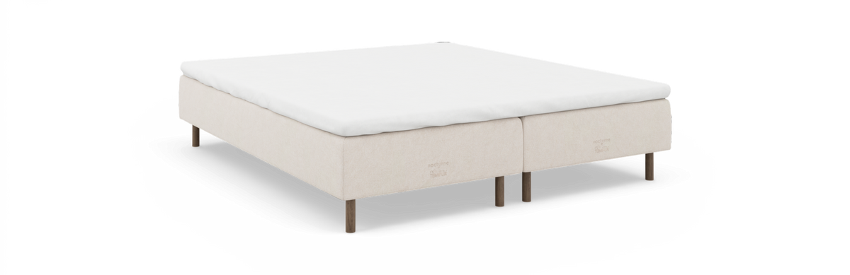 Kontinentalseng i beige med hvid topmadras og træben, ‘nocturne by TEMPUR’ på sengesiden.