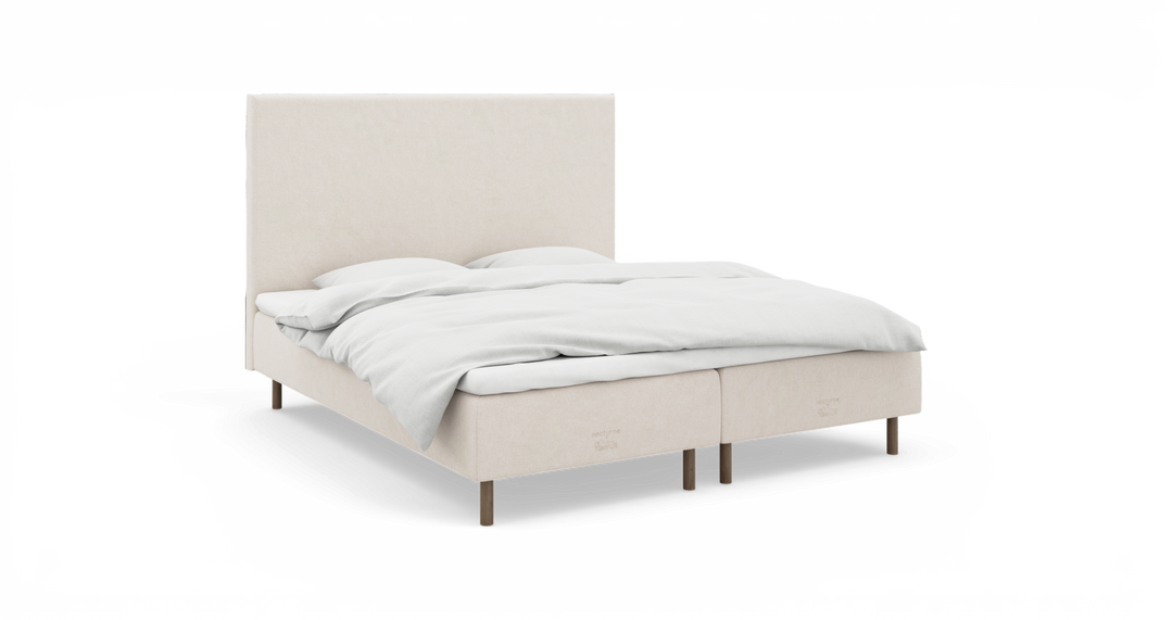 Beige polstret dobbeltseng med høj sengegavl og hvide sengelinned, frilagt mod hvid baggrund set i let frontvinkel.