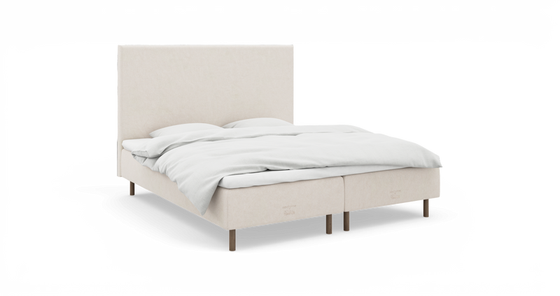 Beige polstret dobbeltseng med høj sengegavl og hvide sengelinned, frilagt mod hvid baggrund set i let frontvinkel._ps