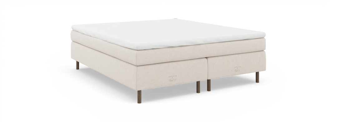 Beige kontinentalseng med hvid topmadras, træben og diskret nocturne by TEMPUR mærkning, set skråt forfra.