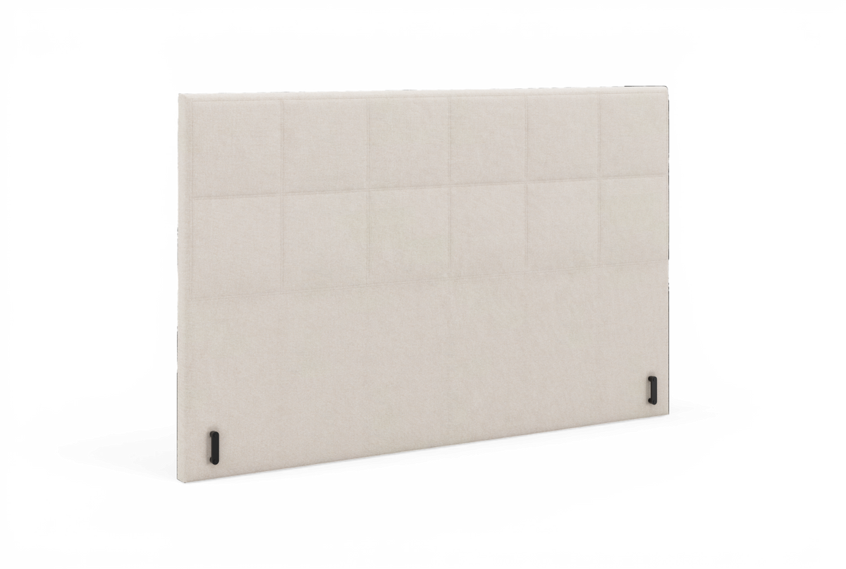 Beige polstret sengegavl i paneldesign, fritlagt.