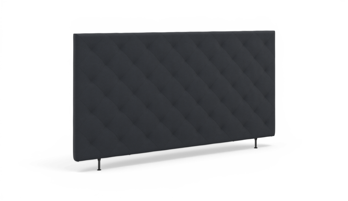 Mørkegrå, diamantquiltet sengegavl med slanke ben på hvid baggrund.