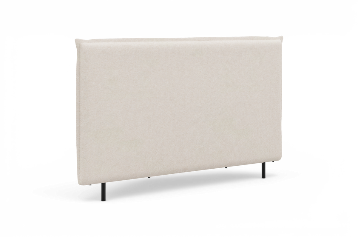 Beige, stofbetrukket sengegavl med slanke sorte ben, fotograferet mod hvid baggrund.