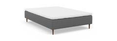 Grå kontinentalseng med hvid topmadras og træben, nocturne, frilagt mod sort baggrund.
