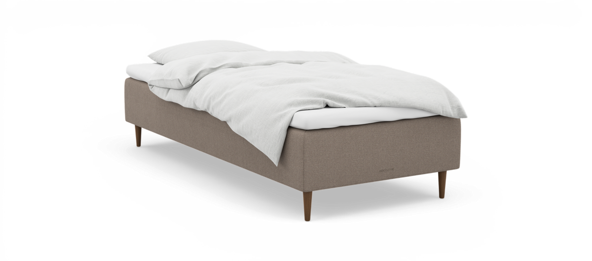 En enkeltseng med beige stofbase, træben og hvidt sengetøj; diskret nocturne‑logo på siden.