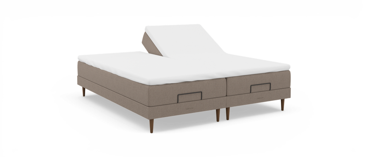 Justerbar dobbeltseng med hævet hovedende på den ene side, beige stofbase og hvid topmadras, frilagt på hvid baggrund.
