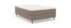 Beige polstret enkeltseng med hvid topmadras, træben og “nocturne”-branding, frilagt på sort baggrund.