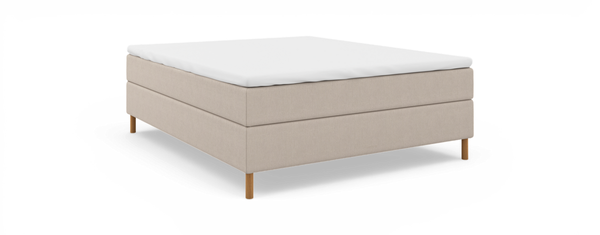 Beige kontinentalseng med hvid topmadras, frilagt mod sort baggrund i skrå frontvisning.