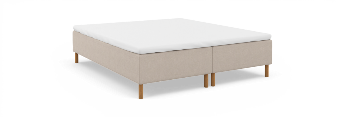 Beige kontinentalseng-base med hvid topmadras og runde træben, frilagt på hvid baggrund.