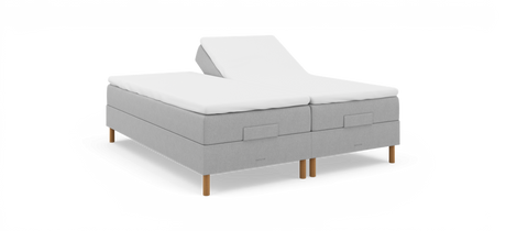 Justerbar dobbeltseng i lysgråt stof med hvid topmadras, træben og logoet nocturne; den ene hovedende er hævet.