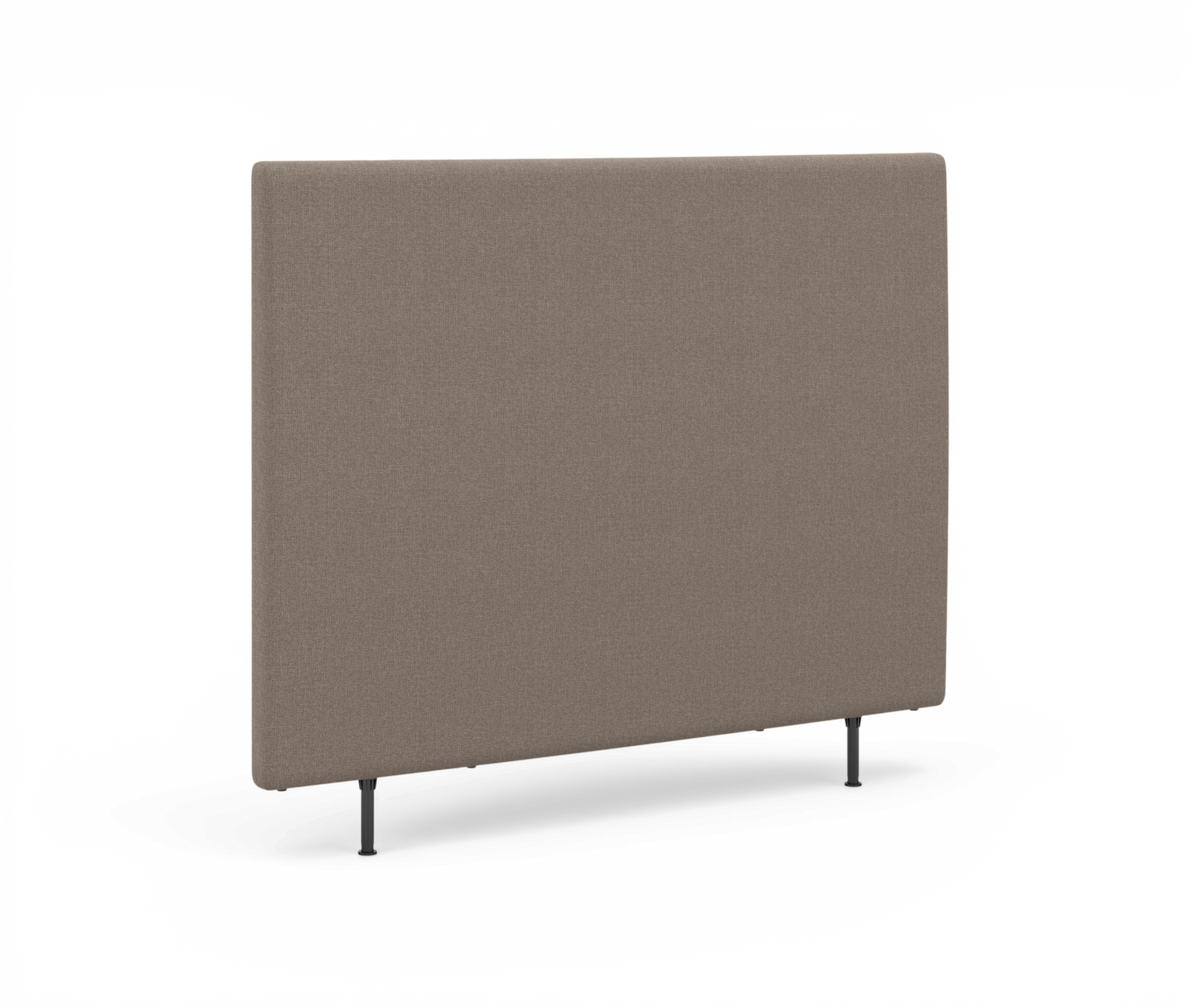 Beige polstret rektangulært sengegærde med slanke sorte ben, fotograferet let skråt forfra.