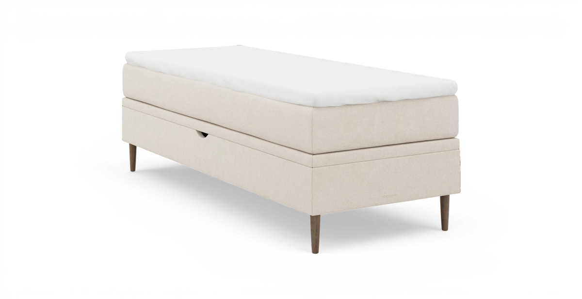 Beige enkeltseng med hvid topmadras og træben, frilagt på hvid baggrund.
