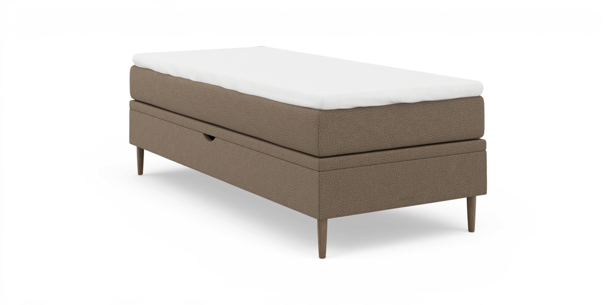 Enkeltseng i beige stof med hvid topmadras og slanke træben, frilagt på hvid baggrund.