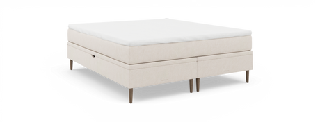 Beige kontinentalseng med hvid topmadras, fritstående mod sort baggrund.