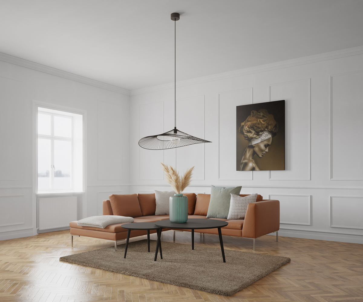 Lyst skandinavisk stue med cognacsfarvet sofa, sort pendellampe, to sorte sofaborde og en grøn vase med pampasgræs på et beige tæppe; vægpaneler og vindueslys samt et portræt-kunstværk med sløret ansigt på væggen.