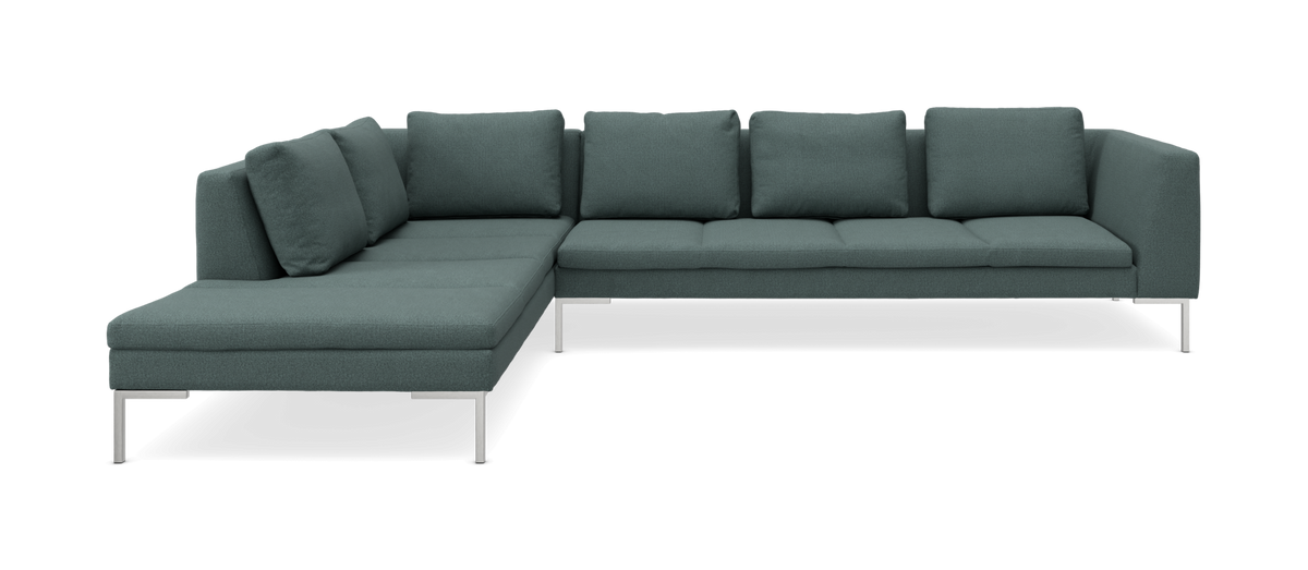 Grøn modulsofa i L‑form med chaiselong og metalben, frilagt på sort baggrund.