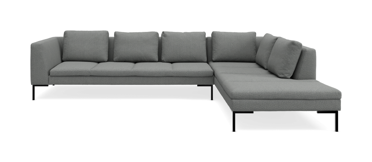 Grå L‑sofa i stof med chaiselong til højre, frilagt på hvid baggrund.