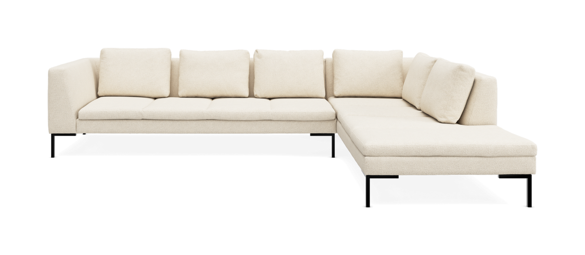 Lysebeige L-formet modulsofa med fem ryghynder og chaiselong til højre på slanke sorte ben.