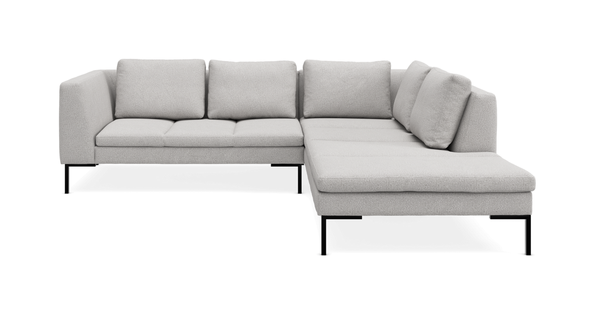 Lysgrå modulsofa i L‑form med chaiselong til højre, slanke sorte ben og løse rygpuder.
