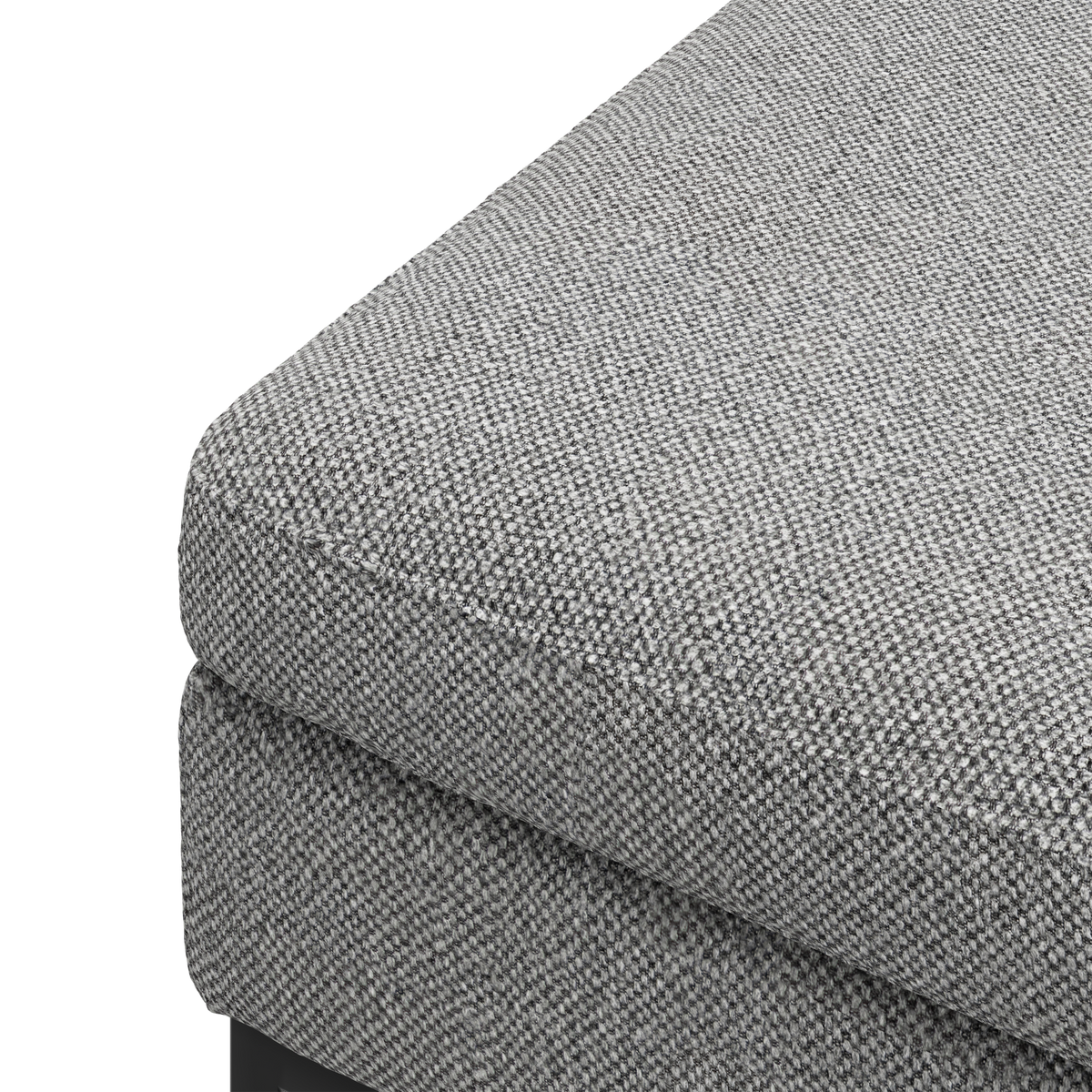 Nærbillede af hjørnet på en grå, tekstureret stofpolstret sofa/ottoman med lagdelt sædehynde.
