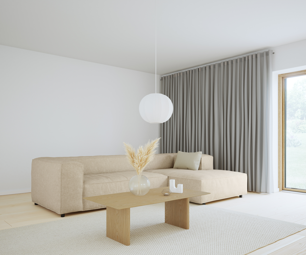 Lyst skandinavisk stue med beige hjørnesofa, lyst sofabord i træ med glasvase med pampasgræs, grå fuldlange gardiner, rund hvid pendel og lyst tæppe ved stort vindue.